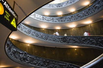Vatican City Museums Tourists descending the Spiral Ramp designed by Giuseppe Momo in 1932 leading from the museums to the street level below seen from below with an illuminated sign warning to watch...