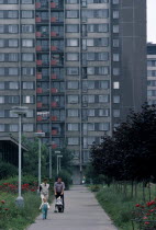 Multi-storey apartment block with young family walking along pathway in foreground.housing residential suburban Ceska Eastern Europe European Flat Immature Kids Praha Young Unripe Unripened Green