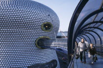 Selfridges Store at The Bullring Shopping Centre. Exterior detail of the spun aluminium discs and shoppers walking through The Parametric Bridge  a curved covered footbridge suspended over the street....