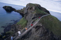 Carrick-a-Rede Rope Bridge. Vistors walking over rope bridge linking a rocky island to cliffs. Originally used by local Salmon fishermen Eire European Holidaymakers Irish Northern Europe Republic Sce...