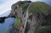 Carrick-a-Rede Rope Bridge. Vistors walking over rope bridge linking a rocky island to cliffs. Originally used by local Salmon fishermen Eire European Holidaymakers Irish Northern Europe Republic Sce...