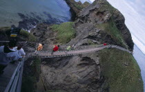 Carrick-a-Rede Rope Bridge. Vistors walking over rope bridge linking a rocky island to cliffs. Originally used by local Salmon fishermen Eire European Holidaymakers Irish Northern Europe Republic Sce...