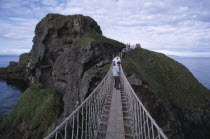 Carrick-a-Rede Rope Bridge. Vistors walking over rope bridge linking a rocky island to cliffs. Originally used by local Salmon fishermen Eire European Holidaymakers Irish Northern Europe Republic Sc...