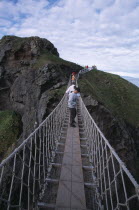 Carrick-a-Rede Rope Bridge. Vistors walking over rope bridge linking a rocky island to cliffs. Originally used by local Salmon fishermen Eire European Holidaymakers Irish Northern Europe Republic Sc...