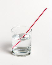 A red and white straw in a glass of water on a white background. The straw appears to be broken  due to refraction of light as it emerges into the aiOptical Illusion Education Educationa Learning Les...