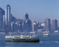 Star Ferries crossing Victoria Harbour with high rise buildings on city skyline beyond. Asia Asian Chinese Chungkuo Jhonggu Zhonggu