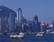 Star Ferries crossing Victoria Harbour with high rise buildings on city skyline beyond. Asia Asian Chinese Chungkuo Jhonggu Zhonggu
