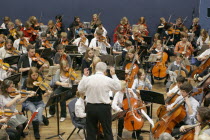 Youth orchestra with conductor in foreground. Sir Michael Tippet giving a music workshop to some young musicians.European Immature Kids Learning Lessons Performance Teaching Public Presentation Young...