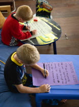 Two young left handed boys on Christmas Eve sitting down and writing their Santa Lists at tablesCultural Cultures Immature Kids Order Fellowship Guild Club Religious West Indies Xmas Christmas Religi...