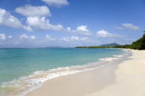 The calm clear blue water breaking on Paradise Beach in LEsterre Bay with Sandy Island  Petite Martinique and High North mountain in the distance and people walking along the sandy shoreCaribbean Gre...