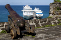 An old canon pointing out to sea at Fort George with two cruise ships the Caribbean Princess and the Aida Aura moored below at the cruise ship terminal in the capital city of St Georges with passenger...