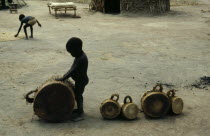 Young son of a drum maker playing with finished drums outside hut.Percussion InstrumentDrumsAfrica African Immature Kids North Africa Southern Sudanese Northern Young Unripe Unripened Green