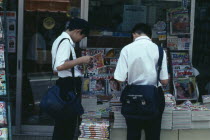 Two Junior High Japanese schoolboys in uniform reading magazines from pavement stand with typical  cute girl  covers.Asia Asian Kids Learning Lessons Nihon Nippon Teaching 2