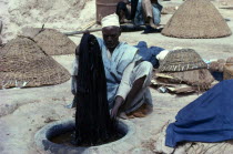 Man dyeing cloth by hand in Indigo dye pits. Vat Clothes Material Colour Colouring Coloring Color Blue Violet African Male Men Guy Nigerian One individual Solo Lone Solitary Western Africa 1 Male Man...