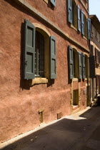 Roussillon.  Typical red exterior wall of building with painted window shutters and step down to street. European French Western Europe