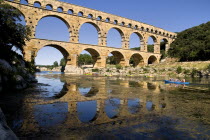 Pont du Gard.  View from west side of the Roman aqueduct in glowing evening light with passing canoes and reflection in water below.Bridge arch European French Western Europe Warm Light
