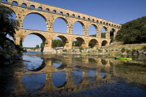 Pont du Gard.  View from west side of the Roman aqueduct in glowing evening light with passing canoes and reflection in the water below.Bridge arch European French Western Europe Warm Light