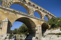 Pont du Gard Roman aqueduct.  Angled view of the east side in the morning showing section of three tiers of arches and rocky bank.Bridge arch stone European French Western Europe
