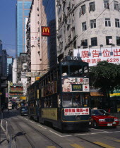 Hong kong Island tram on busy city street with high rise buildings and advertising hoardings.  Sign for McDonalds above tramline.Asia Asian Chinese Chungkuo Jhonggu Zhonggu