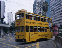 Hong kong Island tram with passengers on top deck looking out of windows  advertising printed along the side and high rise buildings behind.  Asia Asian Chinese Chungkuo Jhonggu Zhonggu