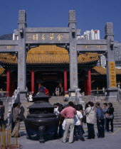 Wong Tai Sin taoist temple established in 1921.  Visitors gathered beside incense burner at foot of flight of steps to entrance built in traditional Chinese style with red interior pillars and pagoda...