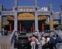 Wong Tai Sin taoist temple established in 1921.  Visitors beside incense burner at foot of flight of steps to entrance built in traditional Chinese style with red interior pillars and pagoda style roo...