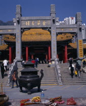 Wong Tai Sin taoist temple established in 1921.  Visitors on flight of steps to entrance built in traditional Chinese style with red interior pillars and pagoda style roof.  Incense  burner and offer...
