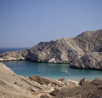 Gulf of Oman. View from coastline over bay with yachts and a schooner on calm blue sea  cliffs behind.Middle East Omani Scenic