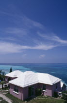 Clifftop house. Purple painted exterior with white roof and view out to sea.  Windswept cloud in blue sky overhead.  Bermudian West Indies