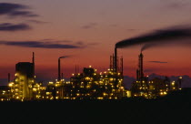 Grimsby petrochemical plant illuminated at dusk.  Buildings and smoke from chimneys silhouetted against  pink and orange sky.Blue Ecology Entorno Environmental Environnement Green Issues