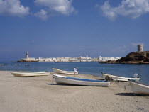 Harbour with boats pulled up on stretch of sand with town and hilltop tower behind.Middle East Omani Scenic
