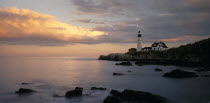 Portland Head lighthouse on rocky headland with blue and gold cloudy sky reflected in calm sea.New England North America United States of America American Great Britain Northern Northern Europe Sceni...