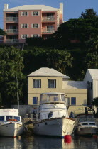 Pink building with white shutters and balconies overlooking boats moored in the water below.Bermudian West Indies