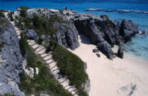 Two people standing on cliff top above empty sandy beach with steps leading down to it at the side. 2 Beaches Bermudian Resort Scenic Seaside Shore Tourism West Indies