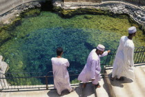 Three men in traditional white dishdashas and brimless  circular hats standing beside hot springs.3 Classic Classical Historical Male Man Guy Middle East Older Omani History Male Men Guy