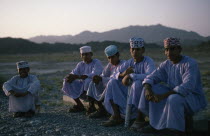 Schoolboys wearing traditional white dishdashas and brimless  embroidered circular hats sitting outside near BahlaClassic Classical Historical Kids Learning Lessons Middle East Older Omani Teaching H...