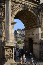 Tourists walking through the triumphal Arch of Septimius Severus with the three remaining Corinthian columns of the Temple of Castor and Pollux in the Forum beyondEuropean Italia Italian Roma Souther...