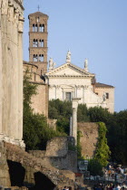 Tourists walking past the Temple of Antoninus and Faustina in the Forum with the belltower and facade of the church of Santa Francesca Romana beyondEuropean Italia Italian Roma Southern Europe Histor...