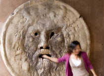 Woman with her hand in the jaws of The Bocca della Verita or Mouth of Truth thought to be a medieval drain cover in the portico of the church of Santa Maria in Cosmedin. Tradition had it that the mout...