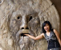 Woman with her hand in the jaws of The Bocca della Verita or Mouth of Truth thought to be a medieval drain cover in the portico of the church of Santa Maria in Cosmedin. Tradition had it that the mout...