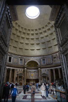 The interior of the Pantheon showing the oculus central opening and the coffering construction of the dome with tourists walking on the patterned marble flooringEuropean Italia Italian Roma Southern...