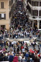 The Via dei Condotti the main shopping street busy with people seen from the Spanish Steps with seated tourists and the Fontana della Barcaccia in the foregroundEuropean Italia Italian Roma Southern...