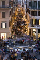 The Via dei Condotti the main shopping street busy with people illuminated at night seen from the Spanish Steps with seated tourists and the Fontana della Barcaccia in the foregroundEuropean Italia I...