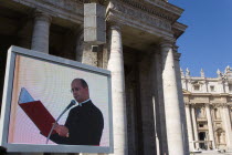 Vatican City A cardinal reading from a red book seen on a large video TV monitor display with Pope Benedict XVI Joseph Alois Radzinger seated under a canopy in St Peters Square for the wednesday Papal...