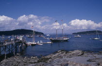 Wooden jetty with approaching yacht  various boats on water and tree covered headland beyond.American Inn New England North America Northern Pub Scenic Tavern United States of America Great Britain N...
