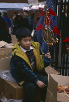 Young boy sitting on boxes holding up decoration for New Year celebrations.Chinese communitysociety ethnic racial diversity Asian European Great Britain Immature Kids Londres Northern Europe One ind...