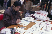 Chinese painter working at stall during New Year celebrations in Chinatown as part of  East Meets West  painting exhibition.Chinese communitysociety ethnic racial diversity Asian European Great Brit...