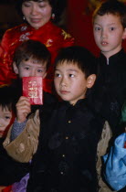 Children celebrating the Year of the Tiger in Chinatown  Soho.  Small boy holding up laisee or lucky packet containing money and decorated with lucky symbols.Chinese communitysociety Asian European...