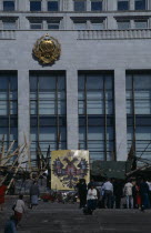 Parliament building with barricades made from pieces of wood and metal after an attempted coup. People standing on the steps next to the Coat of Arms of the Russian Federation emblem which depicts a d...