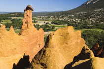 Colorado Provencal.  Cheminee de Fee or Fairy Chimneys.  General vista over smooth  eroded ochre rocks with Rustrel village in distance beyond. Ochre Trail European French Western Europe Scenic
